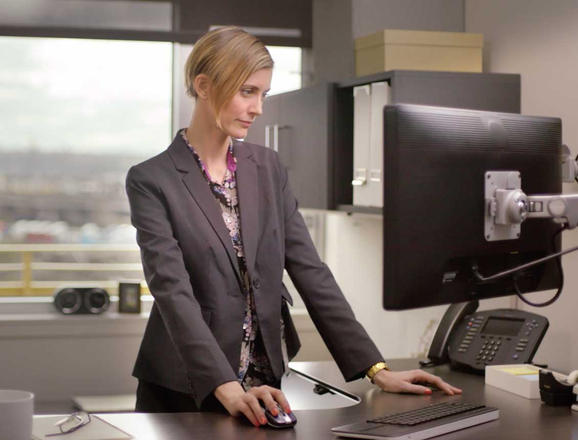A professional woman in her office looking at her computer screen at a stand up desk.