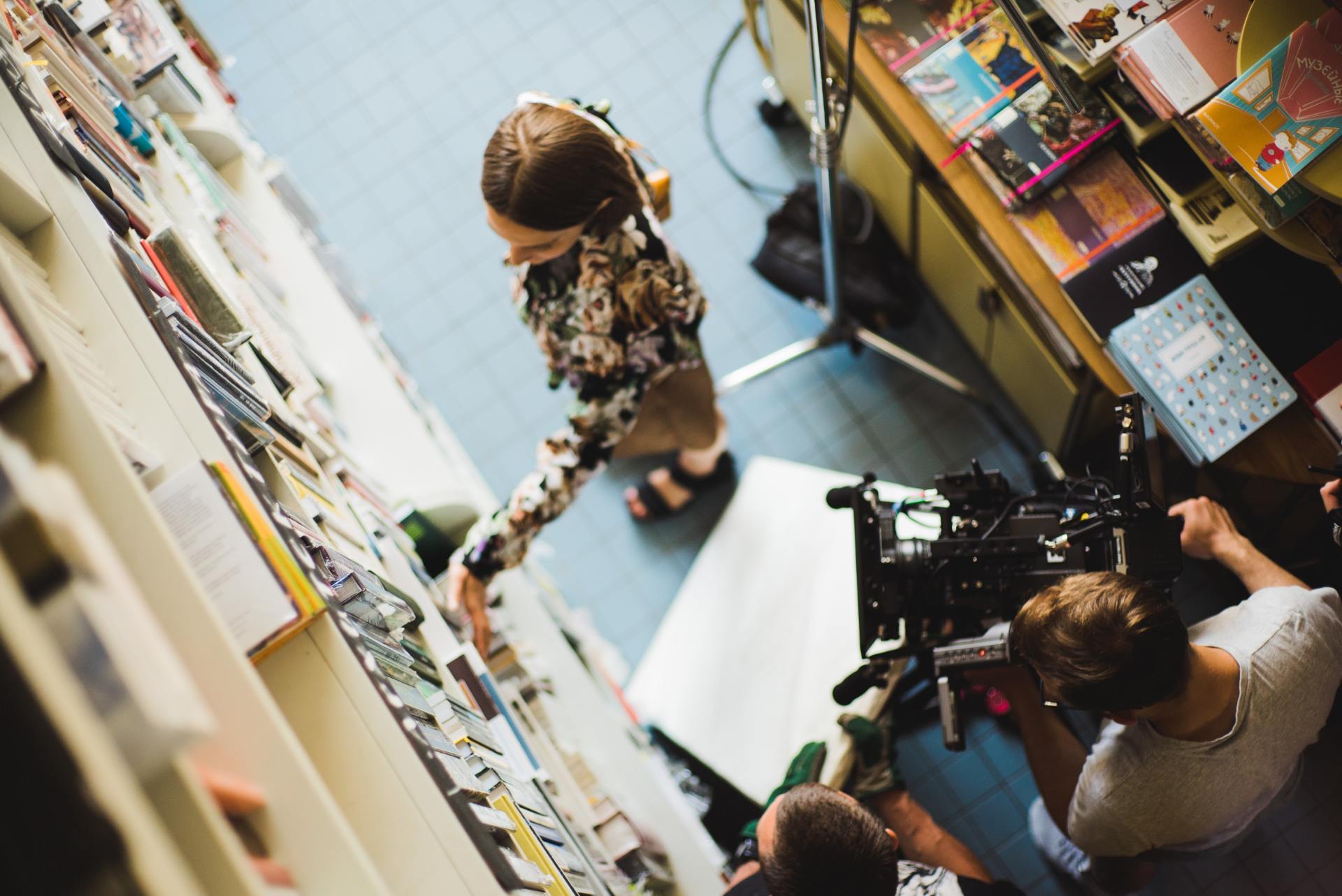 Behind the scenes image of a video production shoot, top down shot of video crew and woman in library.