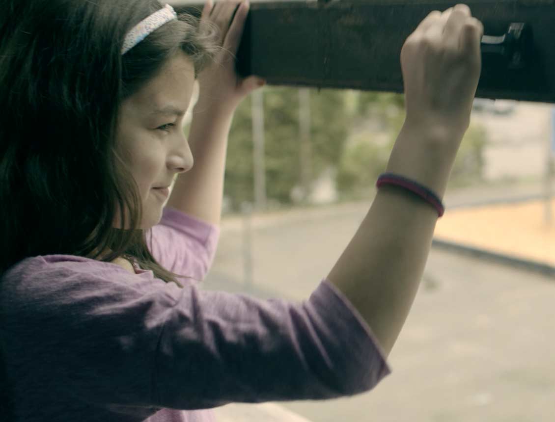 Screen capture image featuring a young girl in a school classroom opening a window and looking out. The image is from a brand film and brand video created for Treehouse, produced by Spin Creative.
