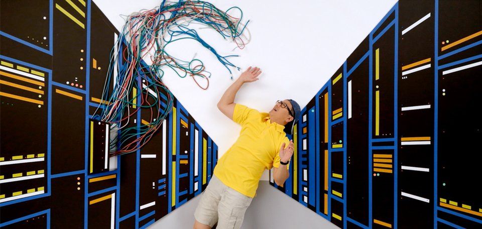 A man in a yellow shirt is standing in a server room.