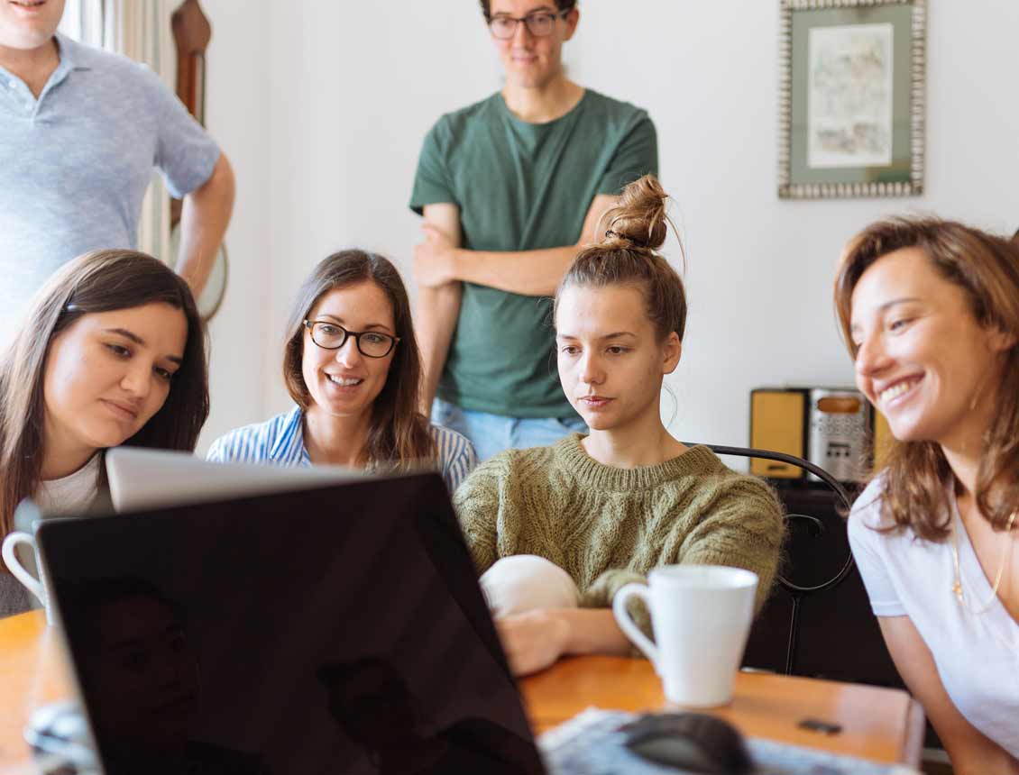 Young women and men gathered around a computer in a house watching long form video marketing content