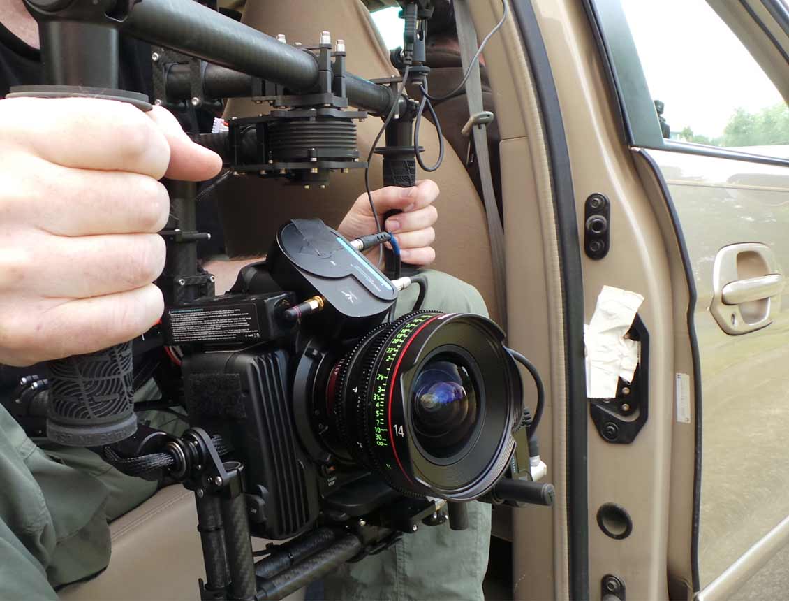 Behind the scenes photo from a Spin Creative video production shoot in Seattle, WA. The photo shows a close up of a MoVi rig mounted with a Canon C300 cinema camera and a 14mm lens behind held out the door of a mini van.