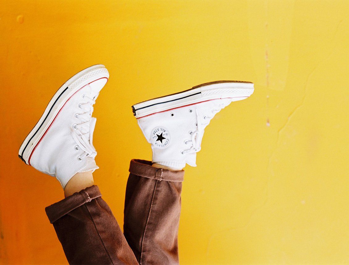 Upside down photo of white high top Converse sneakers against a yellow wall representing the difference between marketing, branding and advertising for Spin Creative blog post.