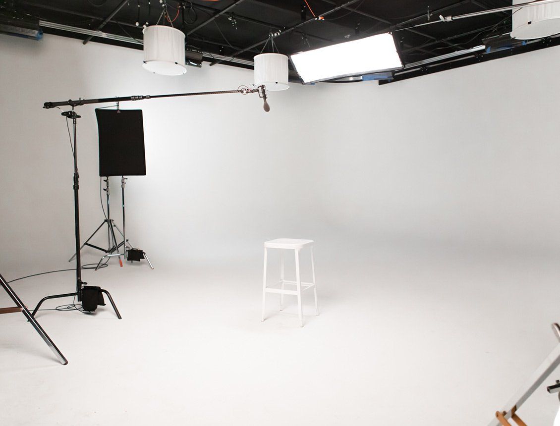 Image of a video production studio and sound stage featuring a white stool, lighting equipment and boom microphone. 