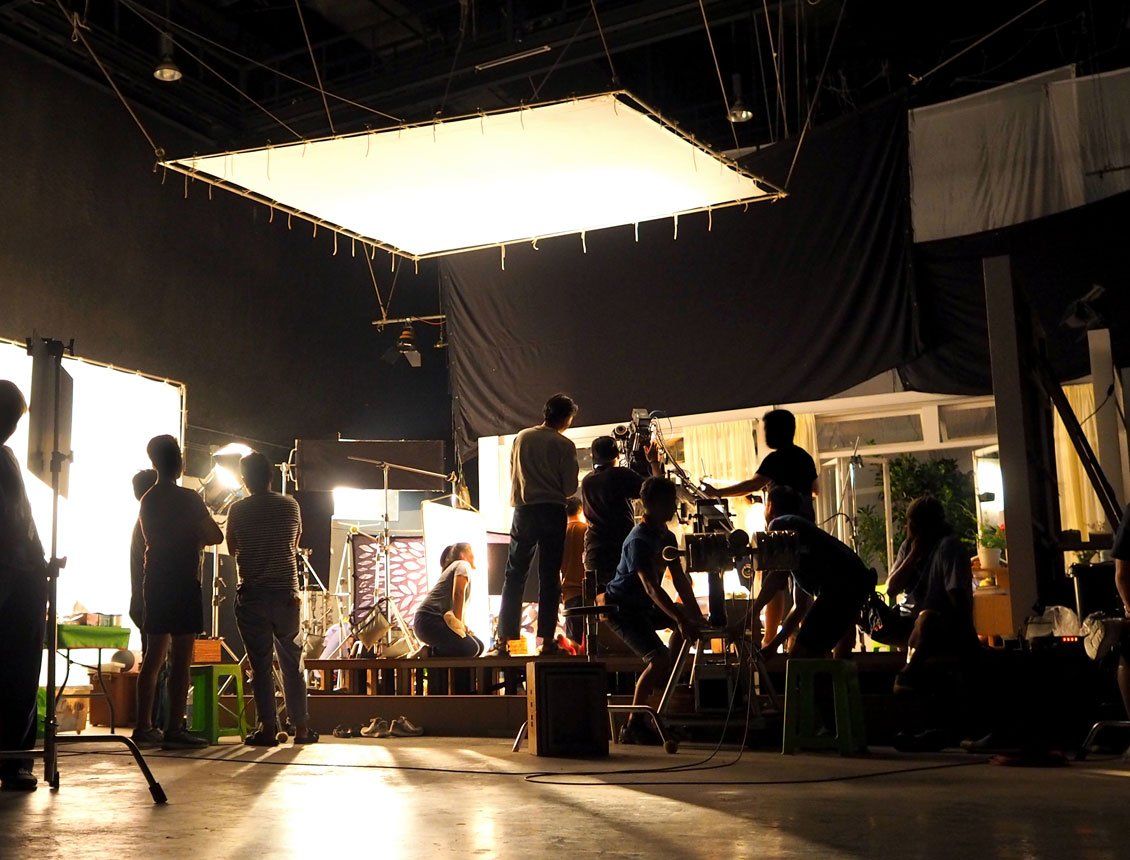 behind the scenes photo of a sound stage or studio featuring a video production crew, large overhead diffusion, a video camera on a jib arm and an interior set constructed to look like the inside of a home.