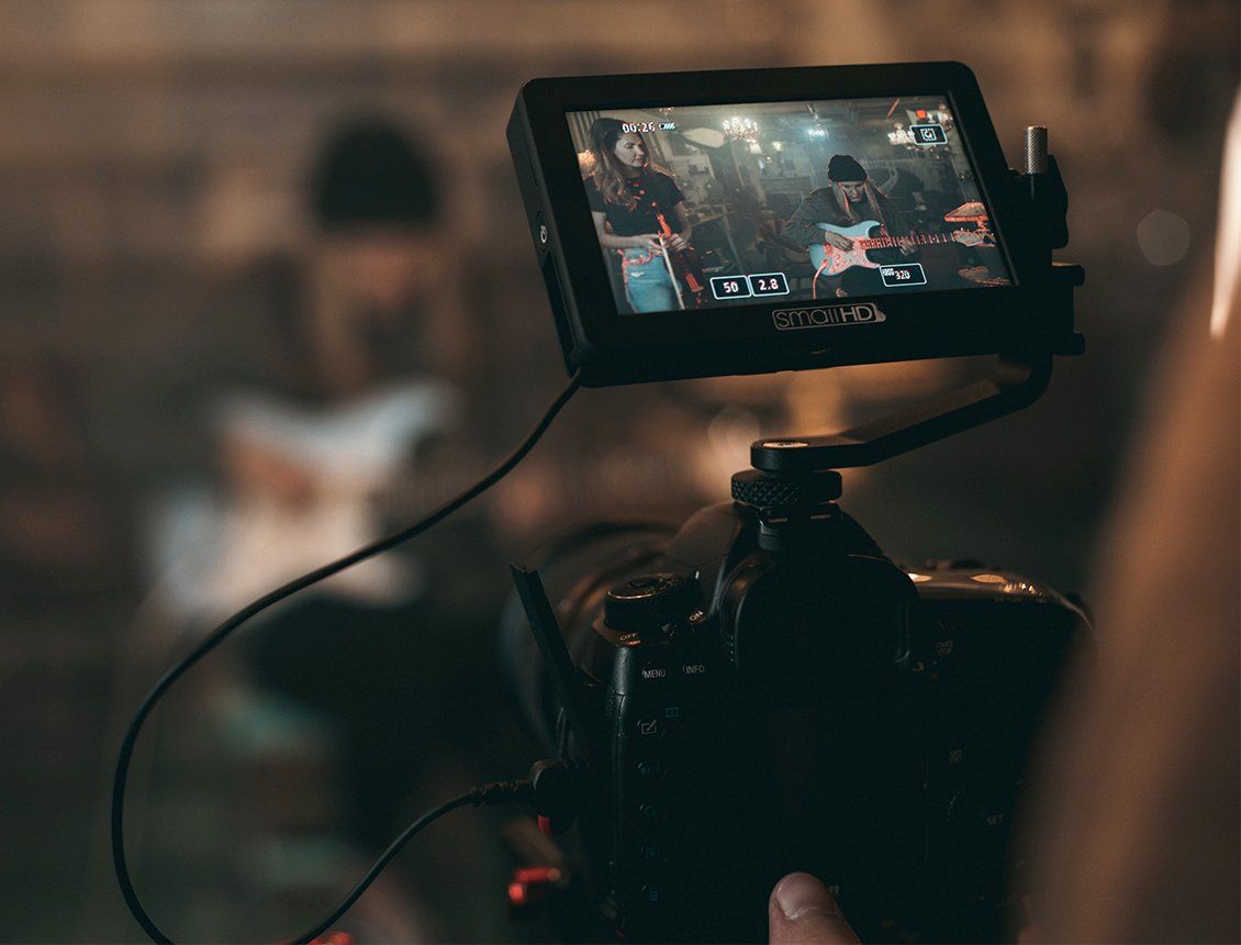 Image of a close up of a DSLR video camera filming a band member playing a guitar. 