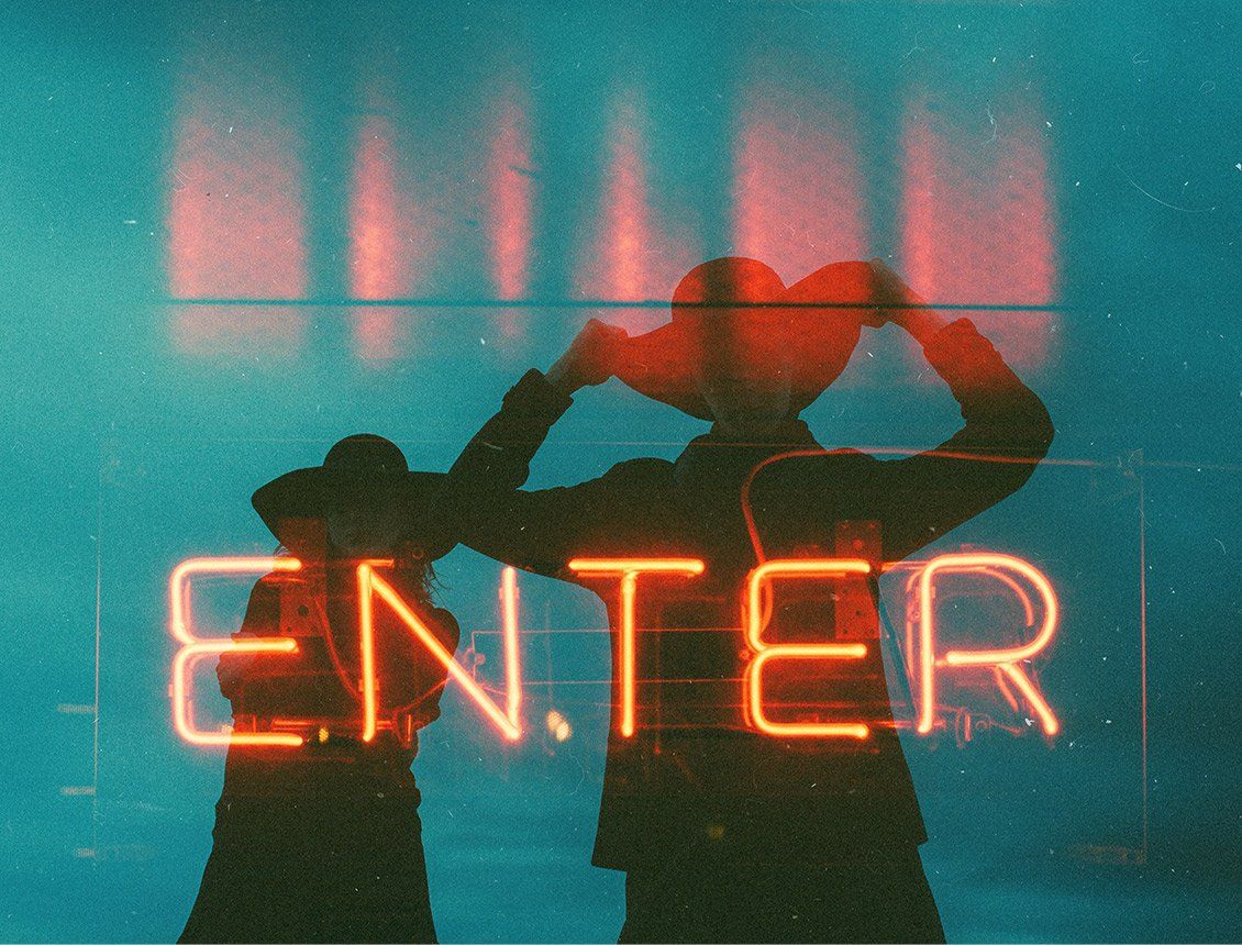 Sillouhette image of two people wearing cowboy hats behind neon