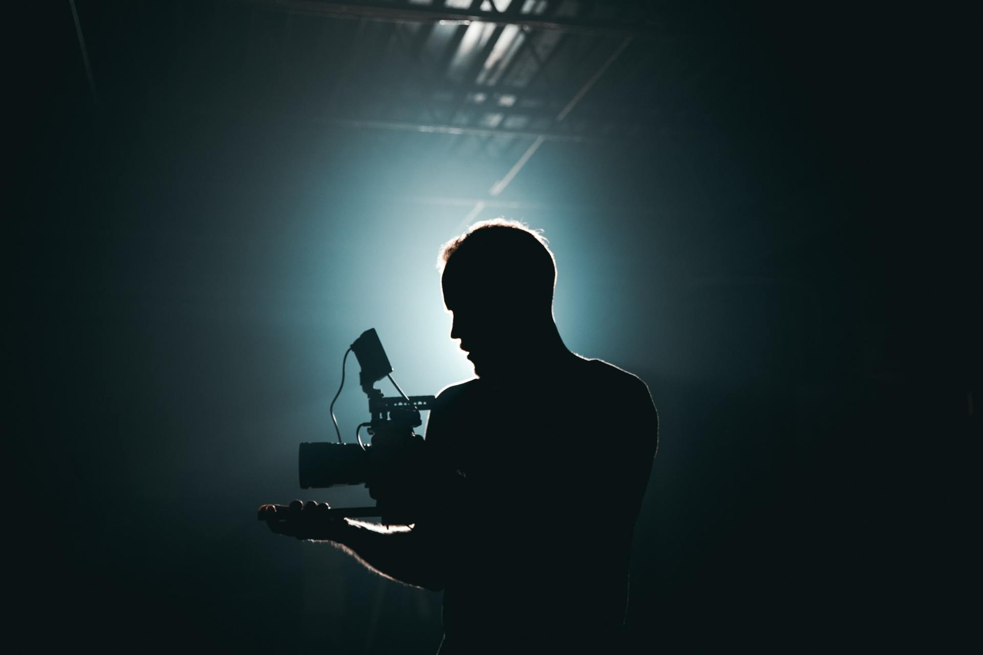 Silhouette of a man hand holding a cinema video camera backlit by a strong light source
