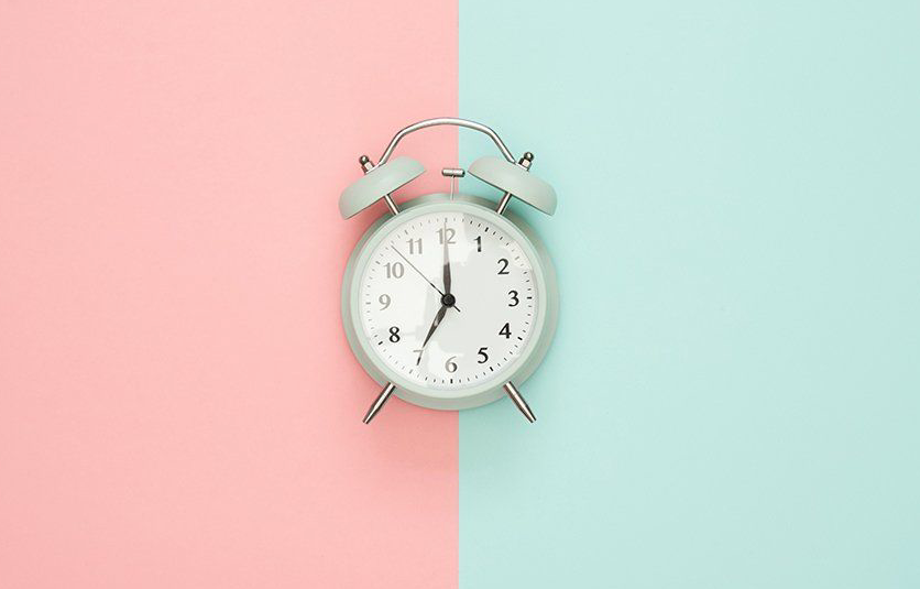 Image of an analog clock over pink and aqua color background