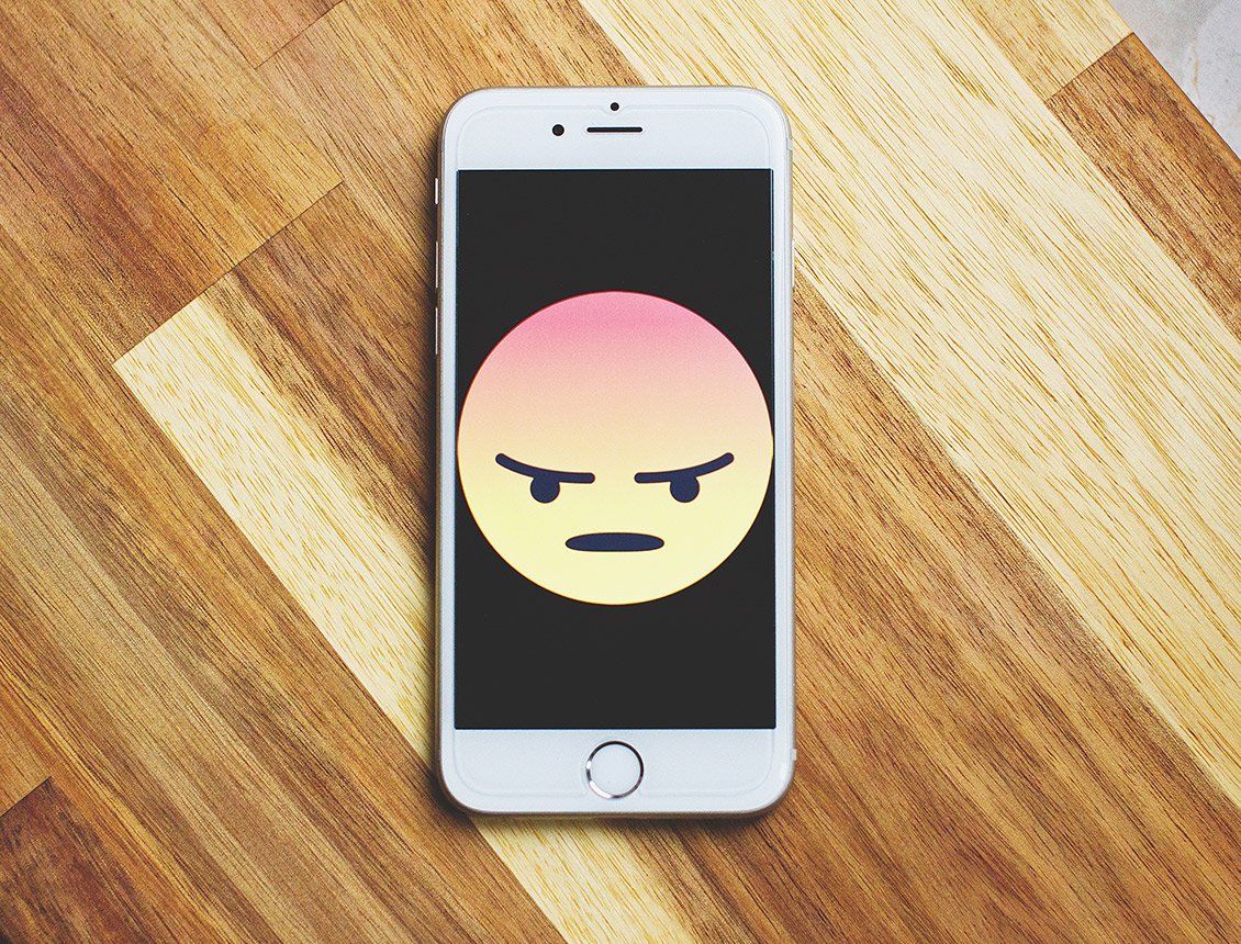 Top down close up of phone sitting on wooden table with sad face on screen
