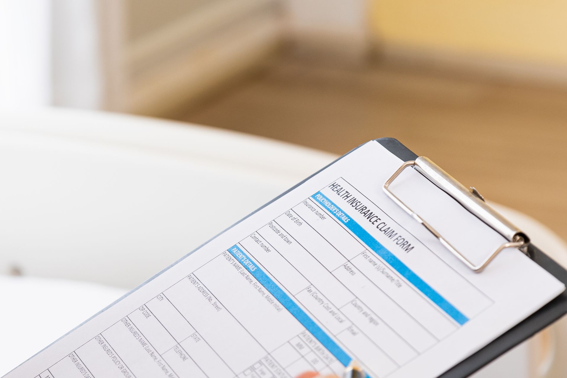 Clipboard with a health insurance claim form, held in a room with a white medical chair. Clipboard with a health insurance claim form, held in a room with a white medical chair.