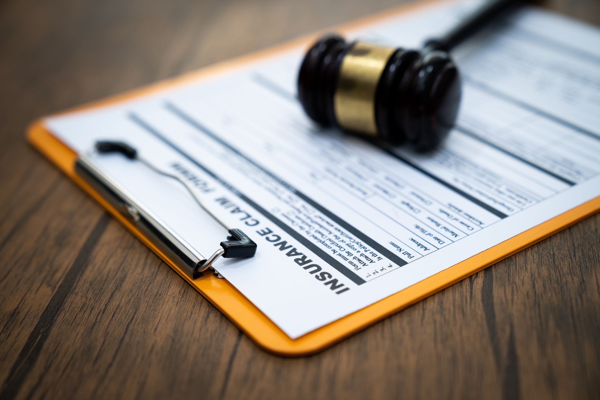 Gavel rests on insurance claim form on clipboard, wooden table background.