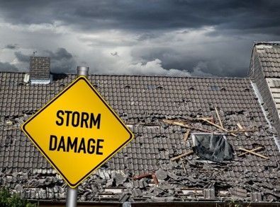 Yellow storm damage sign in front of damaged roof with dark clouds.