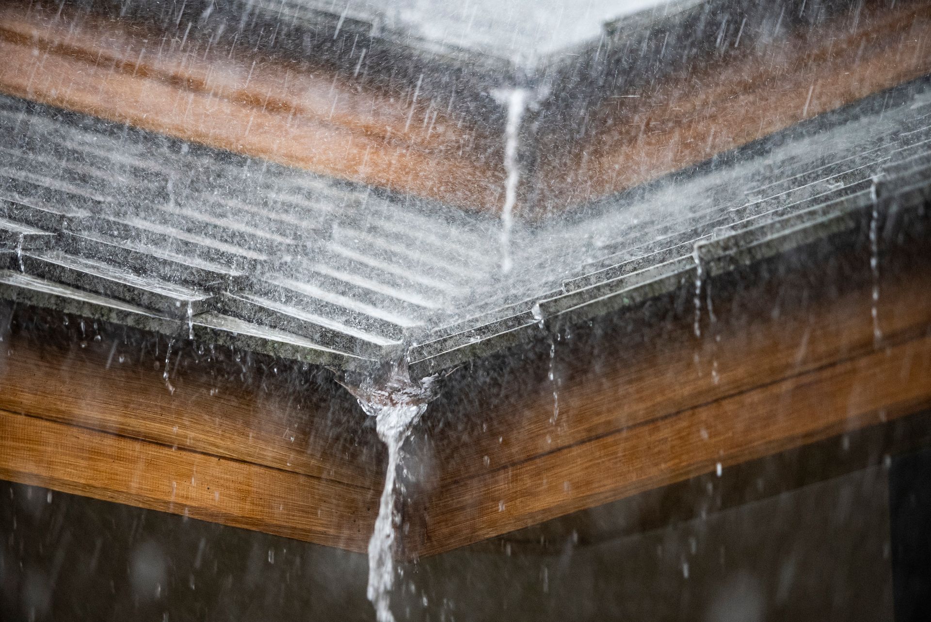 Rain pouring off a roof into a gutter, showing water cascading down and wood framing.