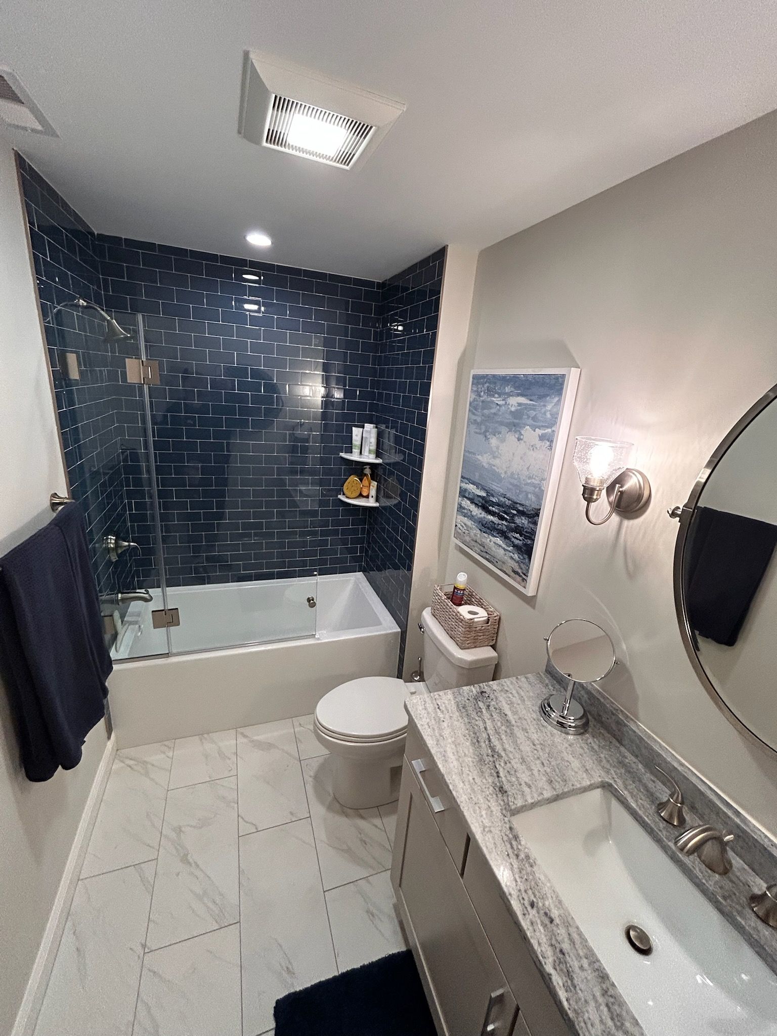 Modern bathroom with blue tile shower, white tub, toilet, vanity, and marble countertop.