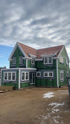Two-story house under construction, green exterior, white window frames, red roof, cloudy sky.