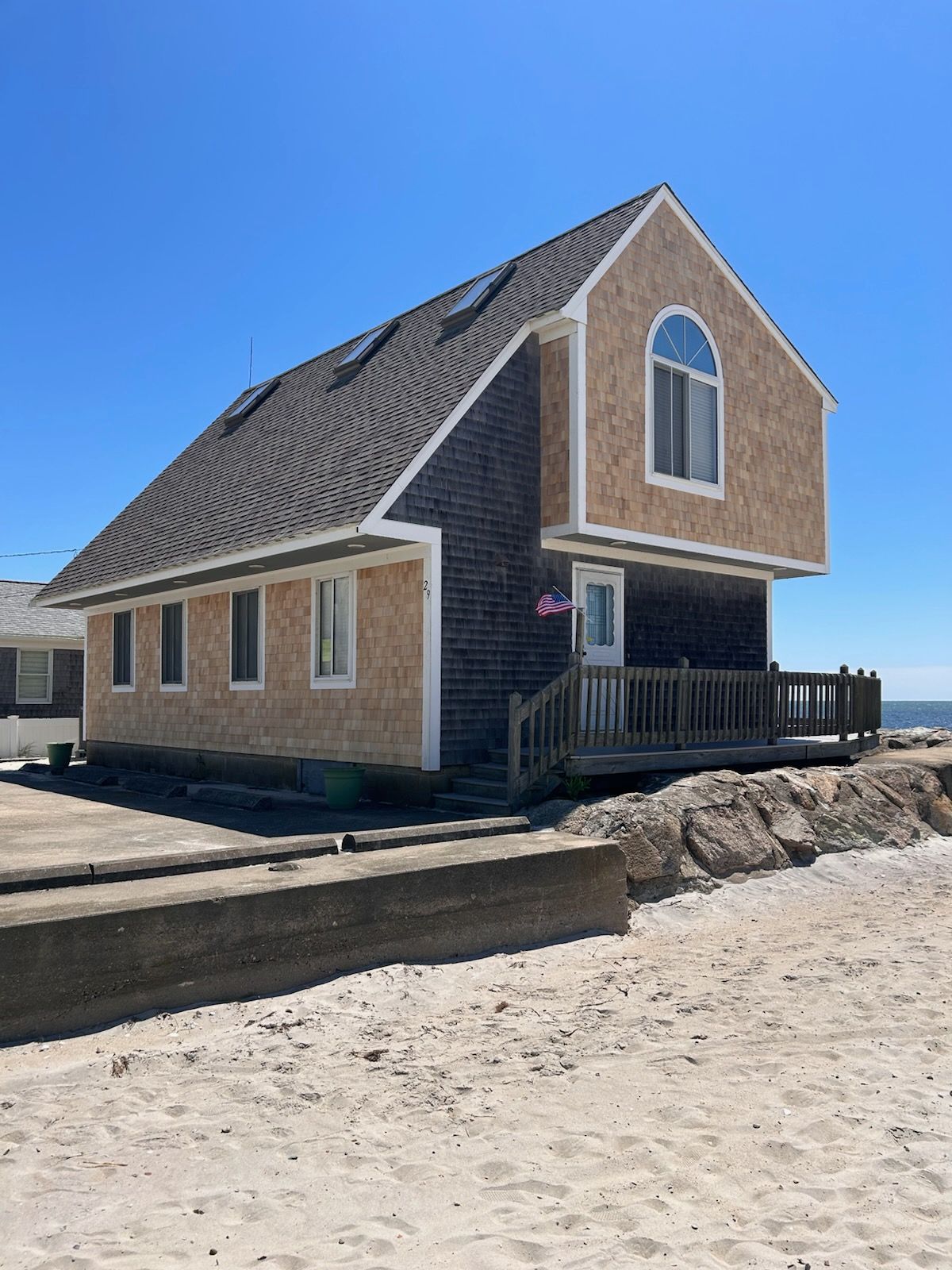 Beachfront house with gray and tan siding, blue sky.