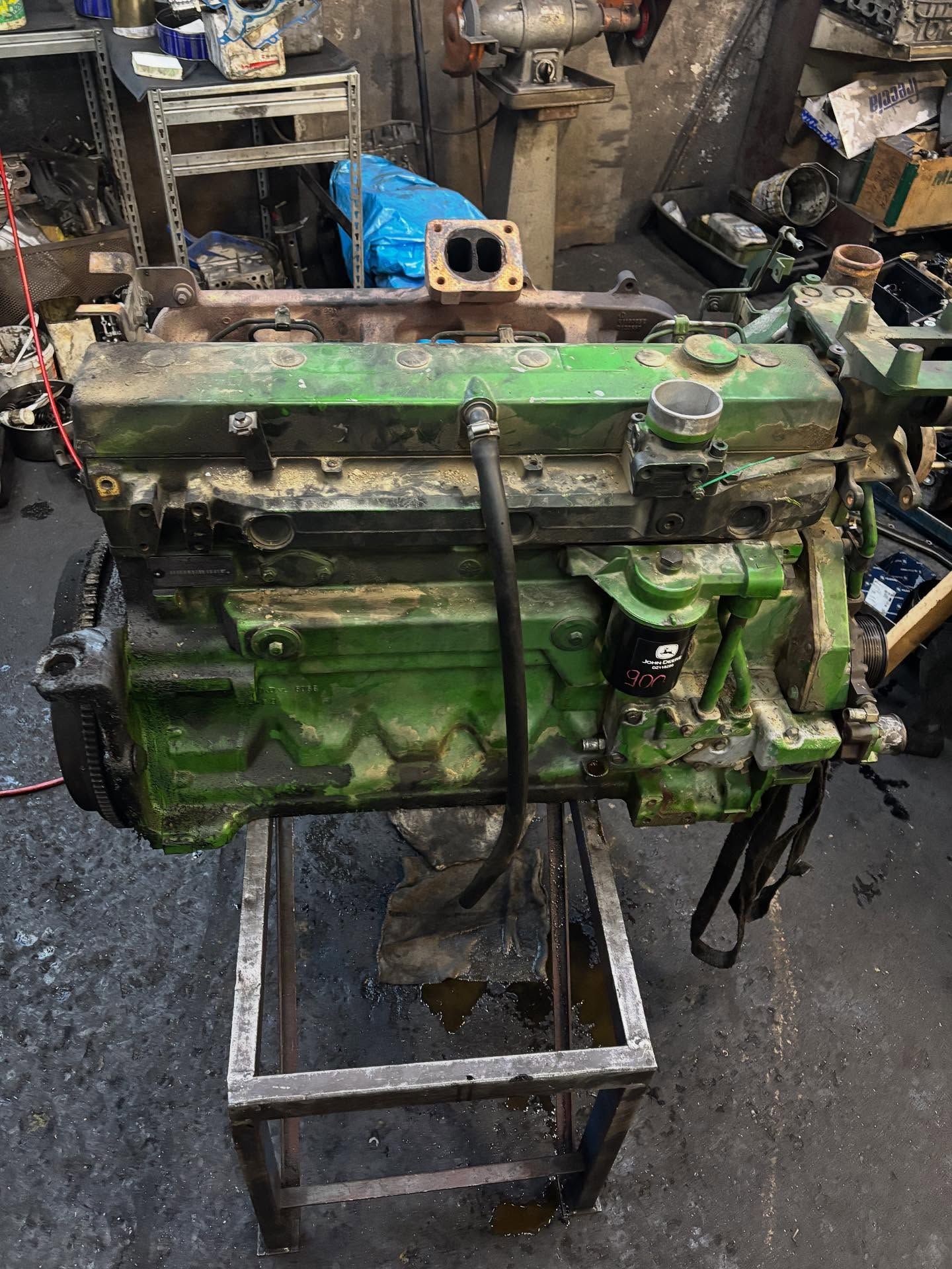 Motore John Deere verde su un supporto metallico in un'officina, coperto di terra.