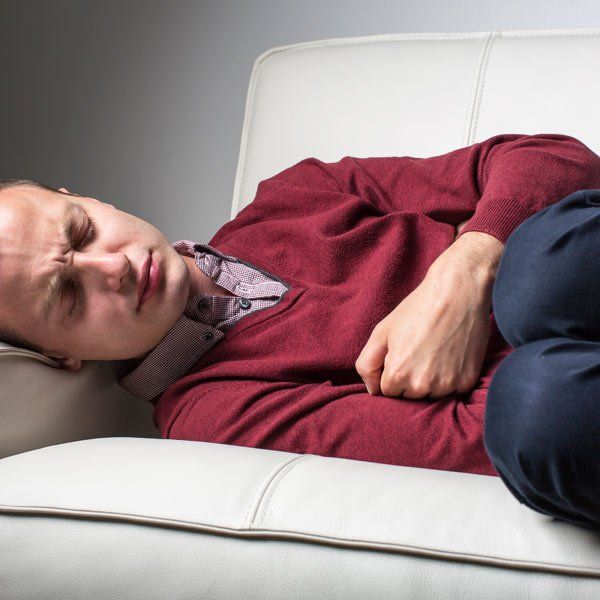 Man with Crohn's Disease laying on the couch with severe belly pain
