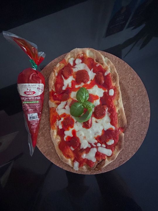 Pizza piatta con salsa, formaggio e basilico, accanto a una confezione di salame.