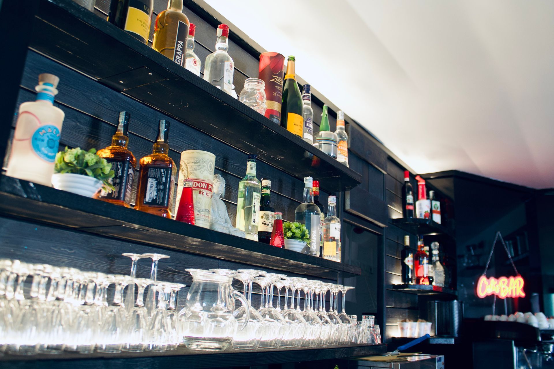 Interno del bar con scaffali pieni di bottiglie di liquore e bicchieri appesi; sfondo nero.