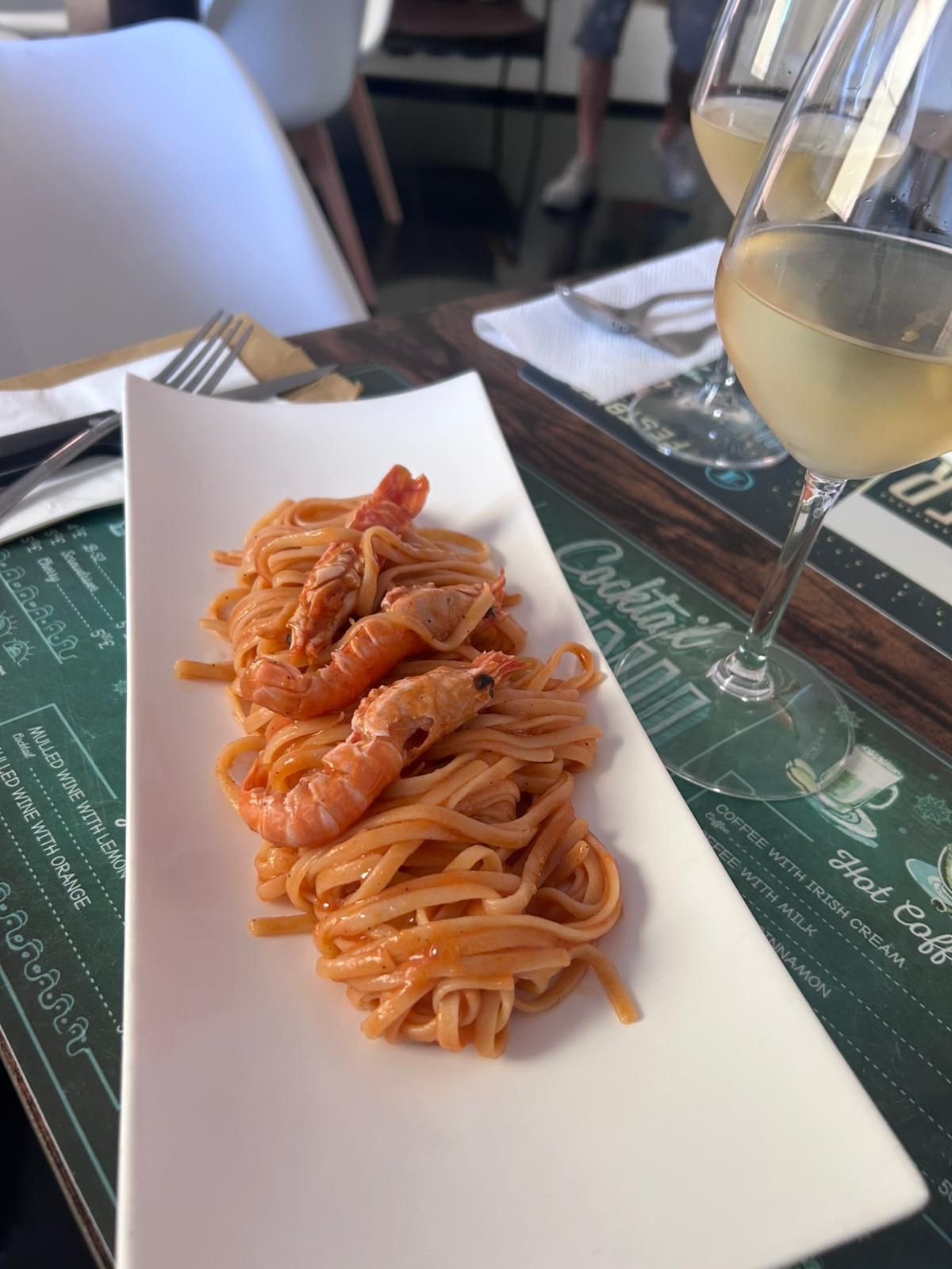 Zona pranzo con sedie bianche, tavolo in legno e una parete verde.