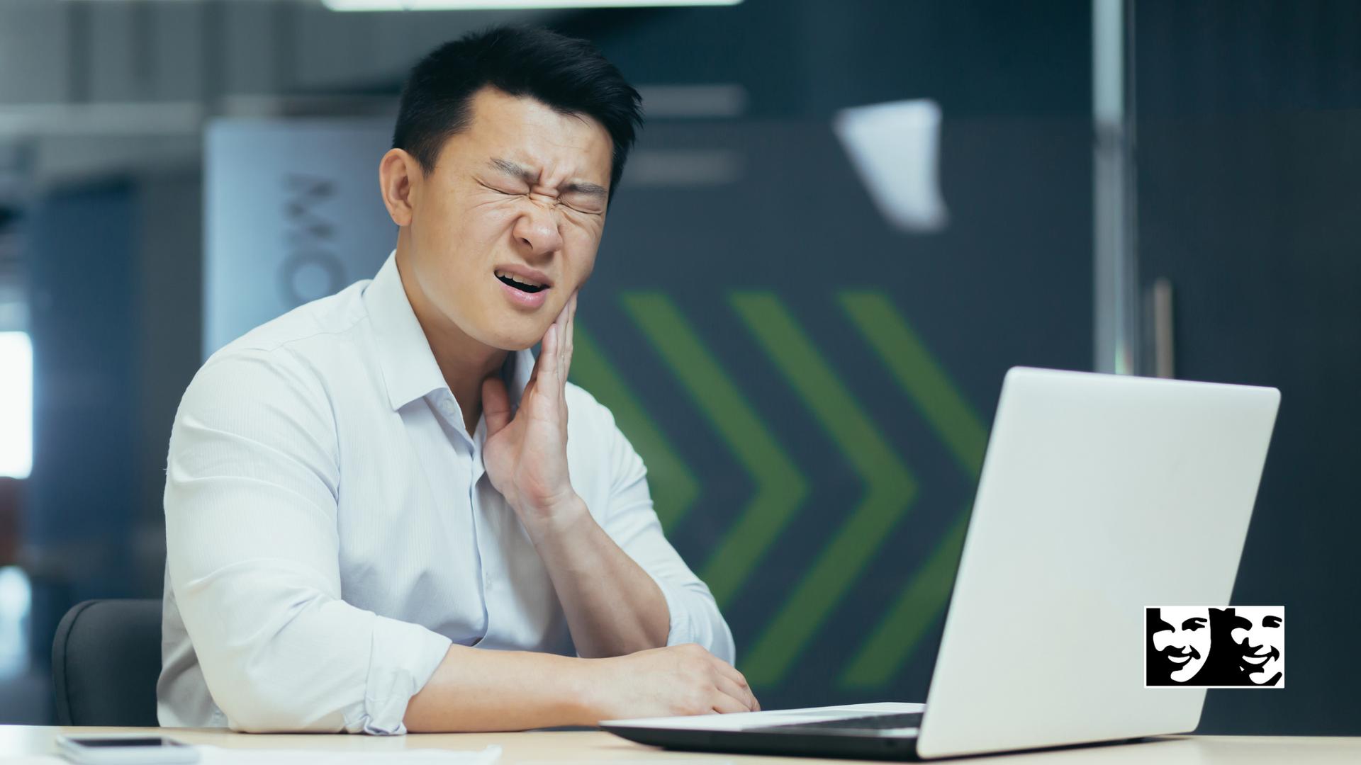 A man is sitting in front of a laptop computer with a toothache.