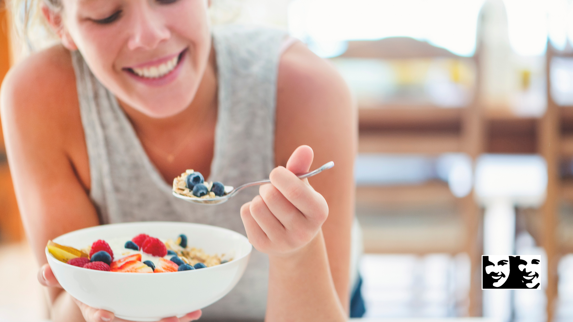 Woman smiling, eating cereal with berries in a white bowl, inside a home.