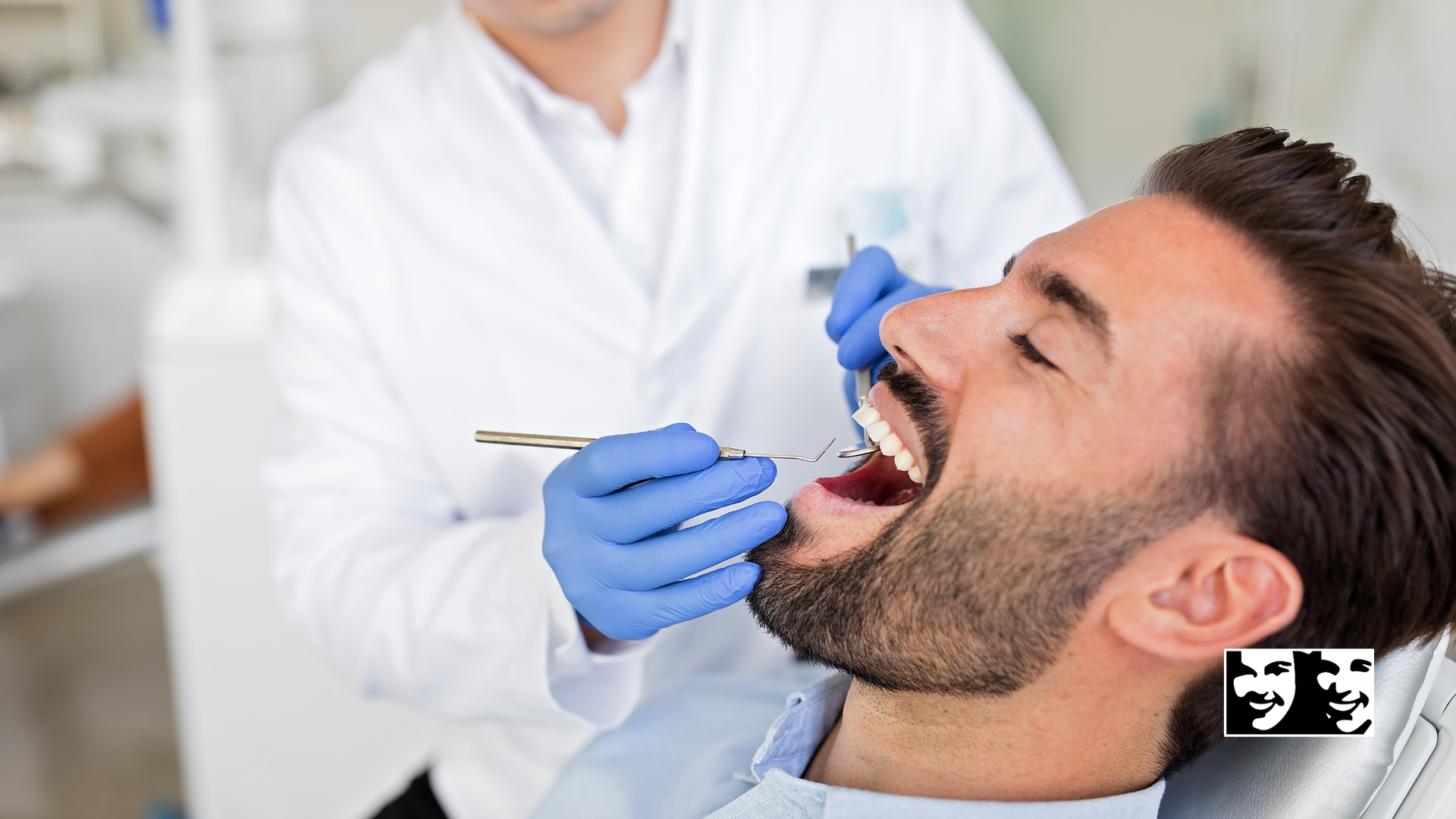 Man in dental chair with mouth open as dentist examines teeth with instruments.