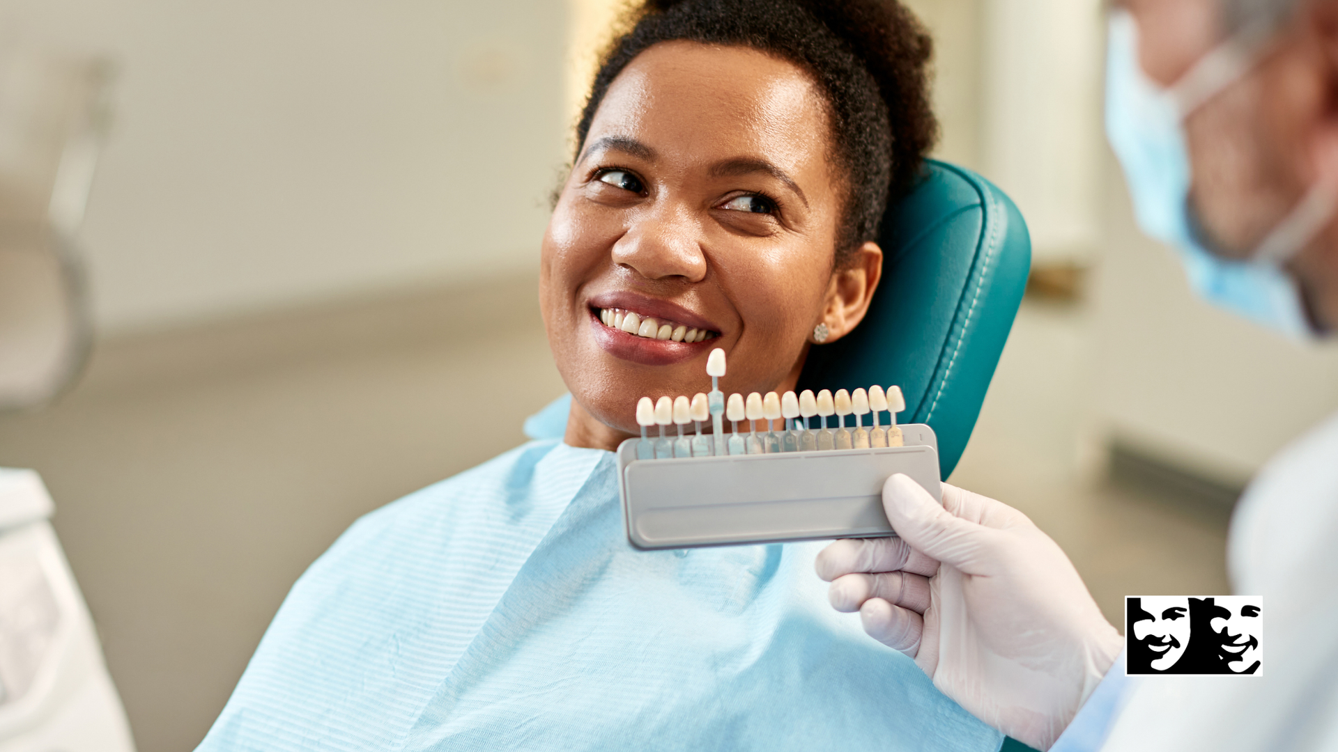 A woman is sitting in a dental chair while a dentist holds a tooth color chart.