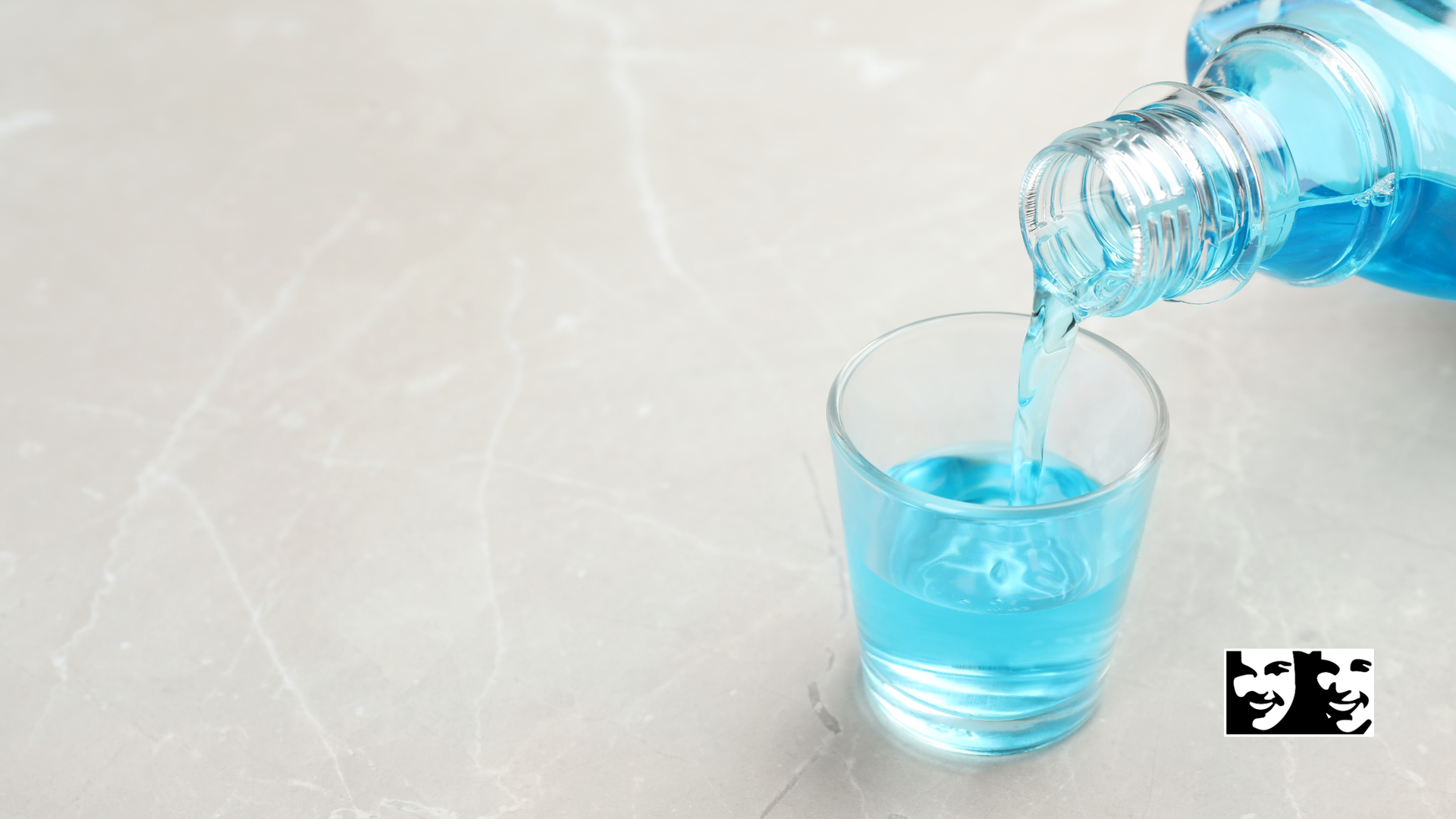 Blue mouthwash pouring from a bottle into a small glass.