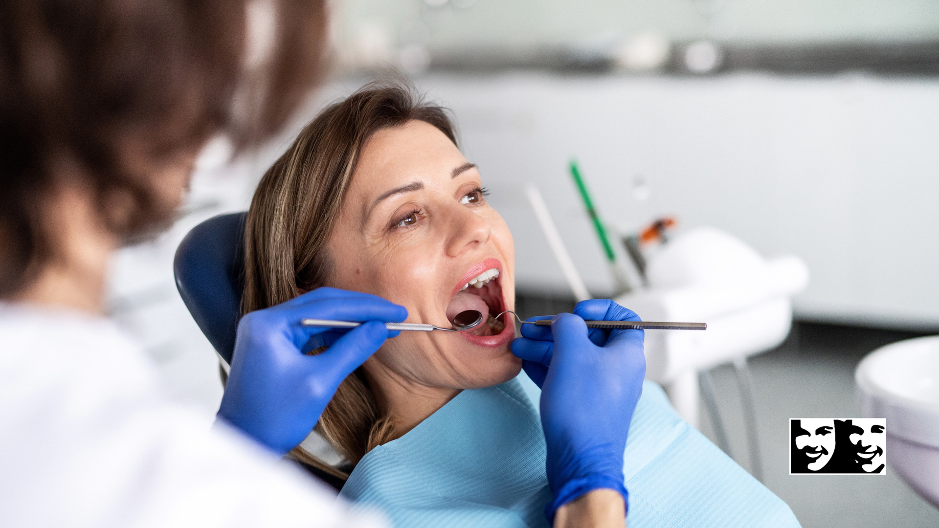 Dentist examining patient's mouth with tools; blue gloves, white chair, bright lights.