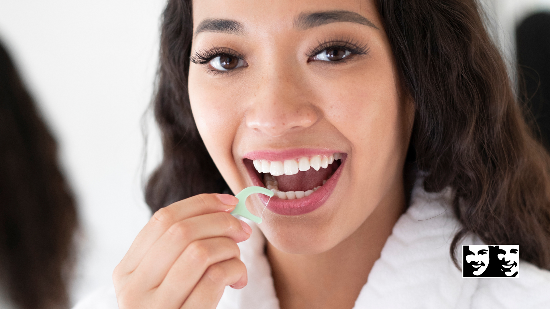 A woman is brushing her teeth with a floss in front of a mirror.