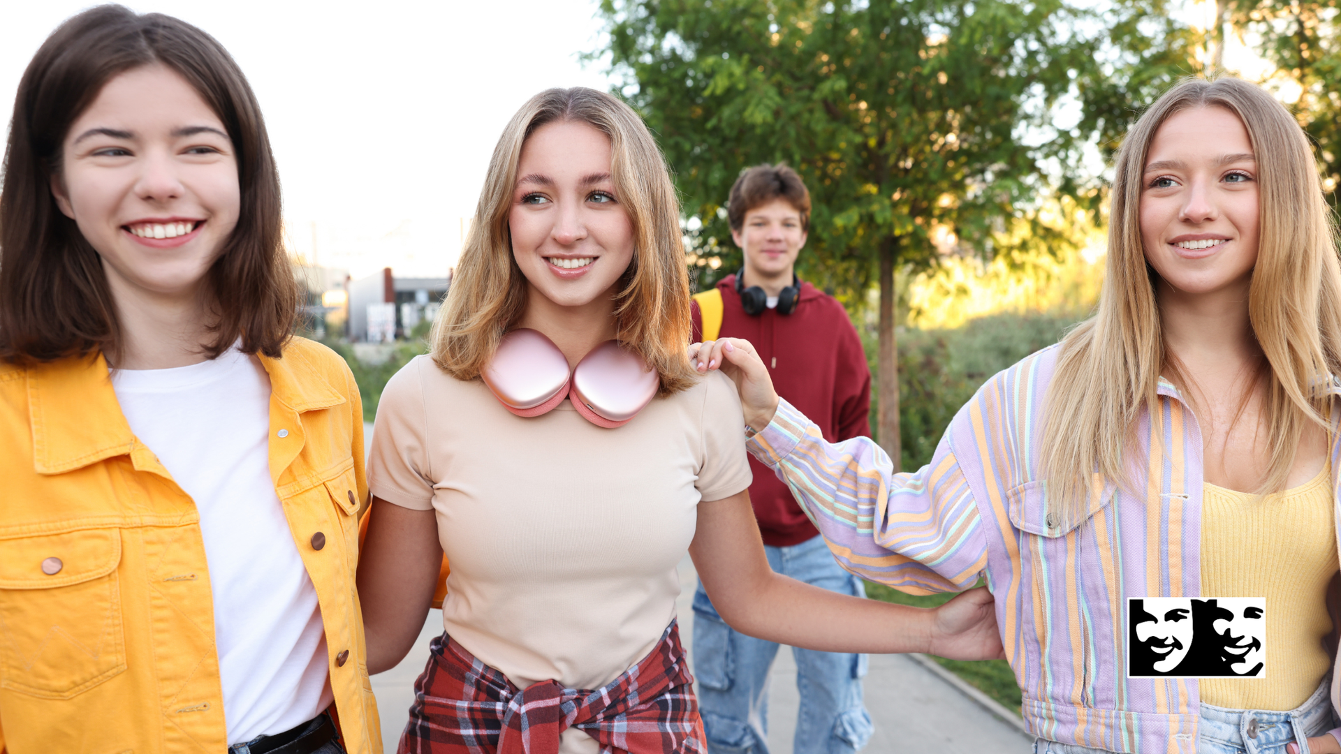 Four smiling people huddle together under a blue sky, arms around each other, looking down.