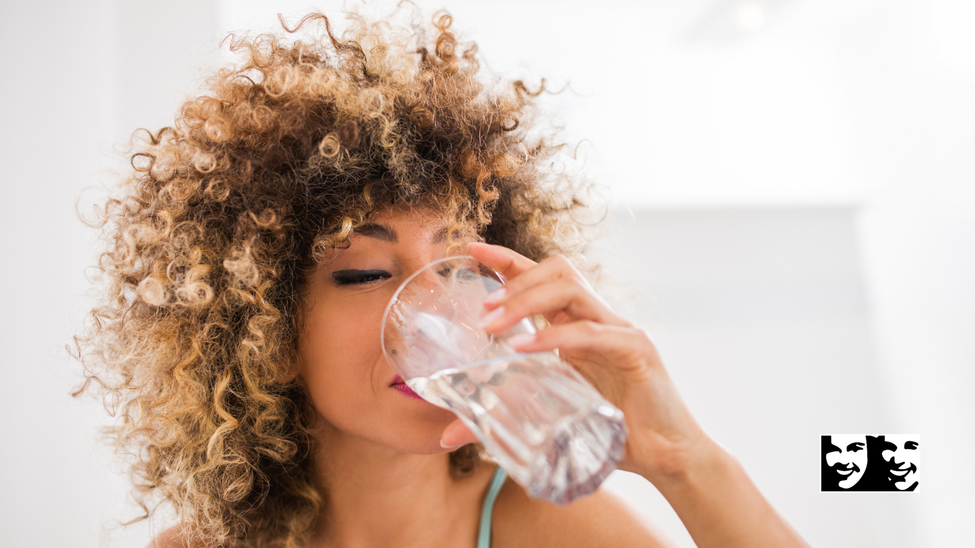 A woman with curly hair is drinking water from a glass.