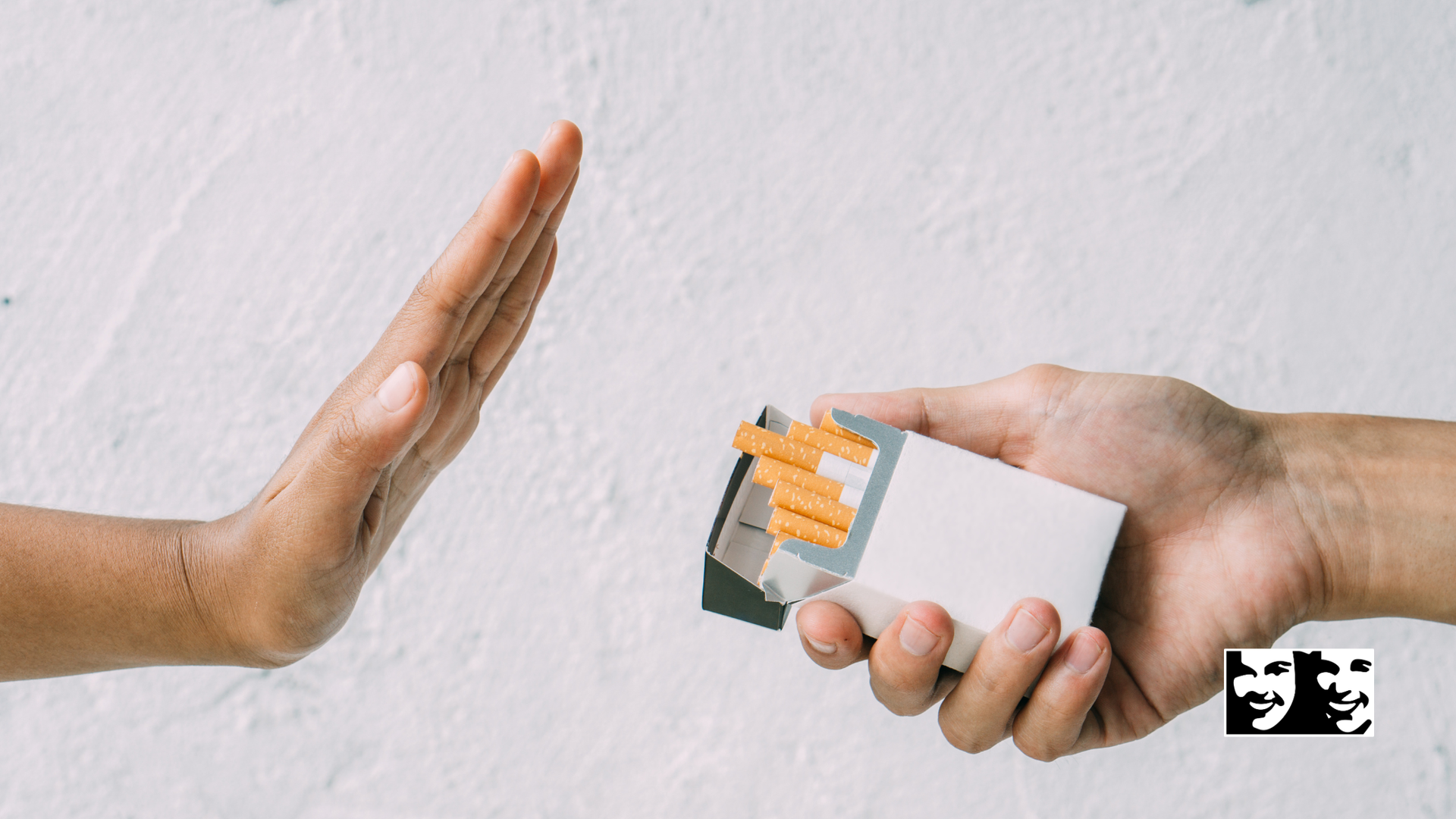 Hand rejecting a cigarette pack, against a white wall.