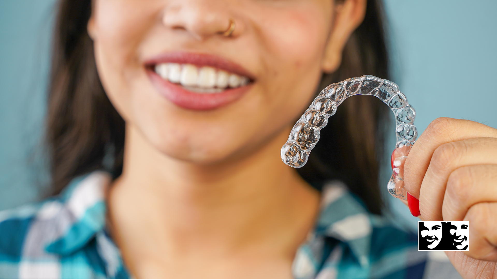 Person holding clear aligner, smiling, preparing to put it in mouth.