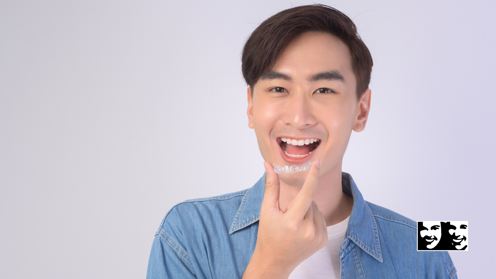 A young man is smiling and pointing at his teeth.