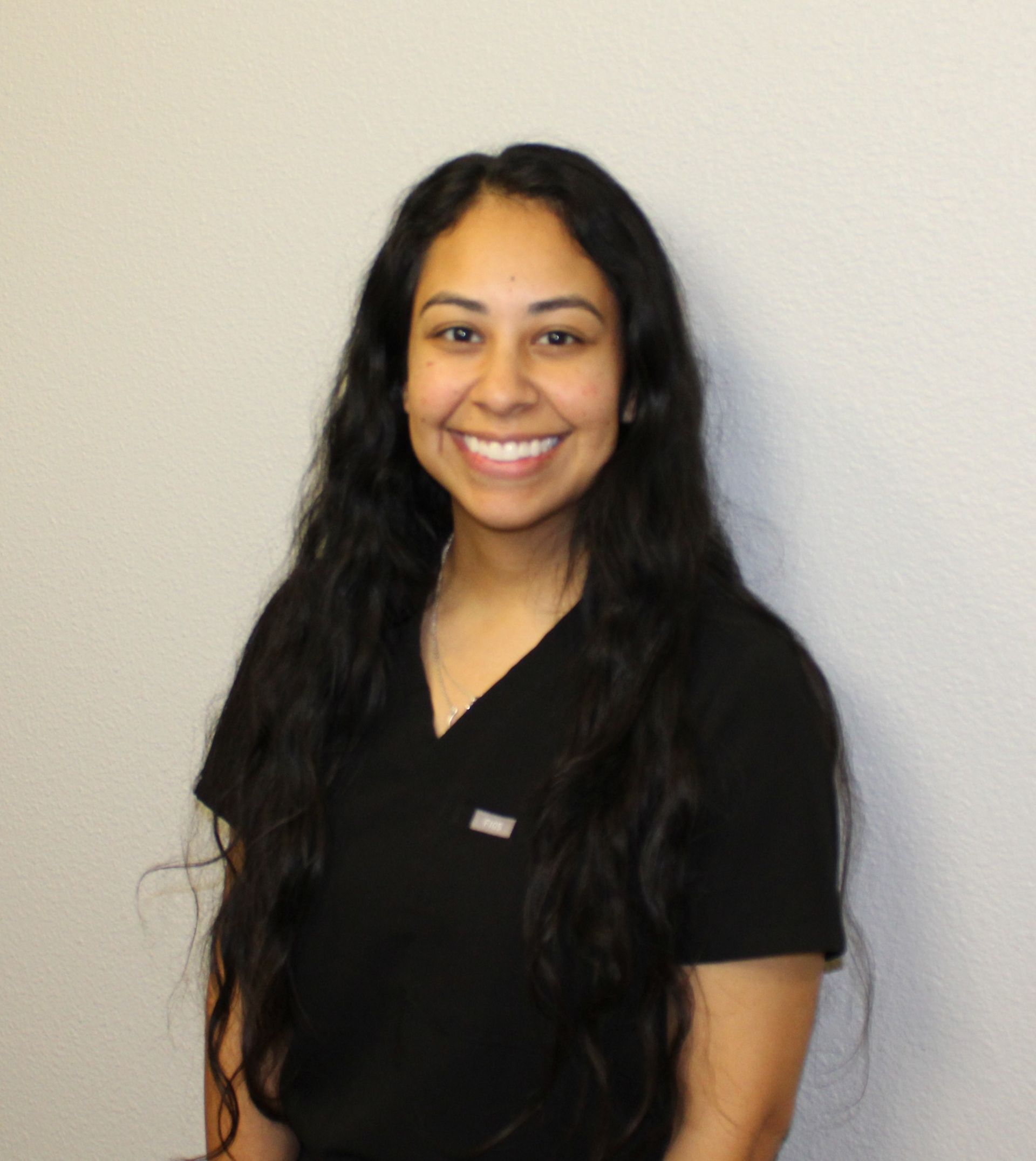 A woman in a black shirt is standing in front of a white wall.