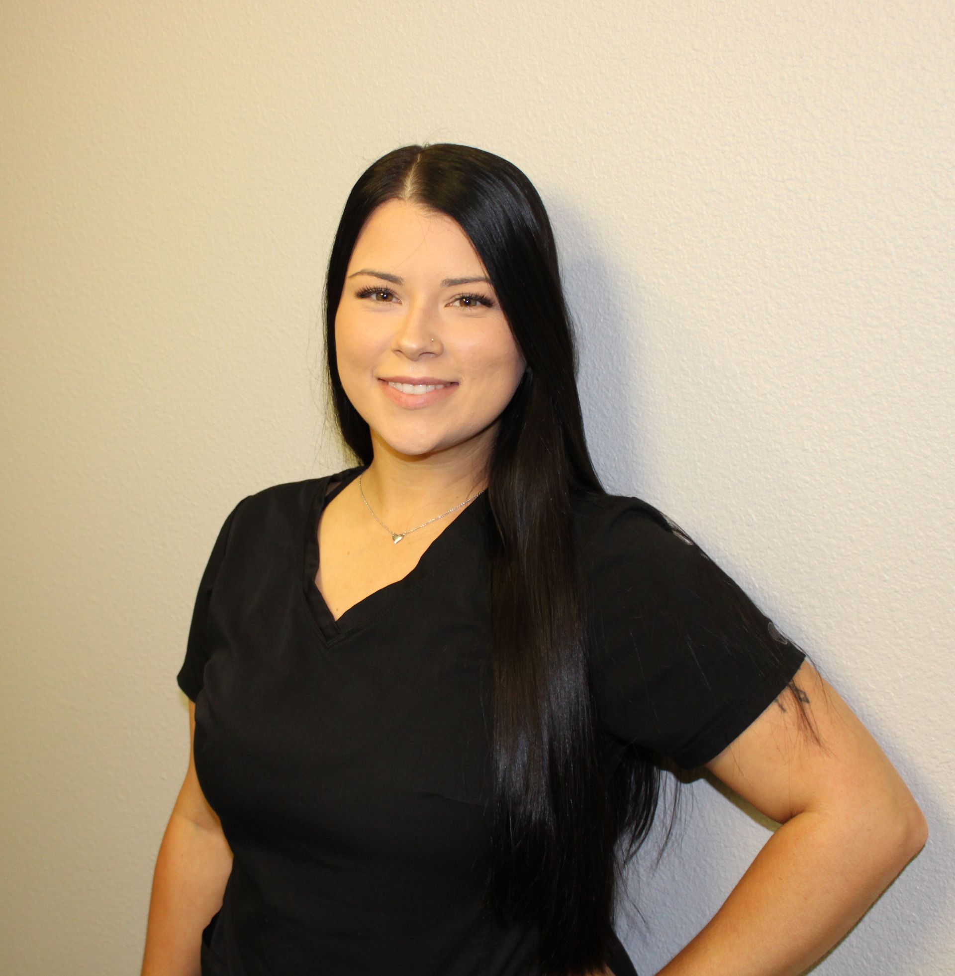 A woman in a black shirt is standing in front of a white wall.