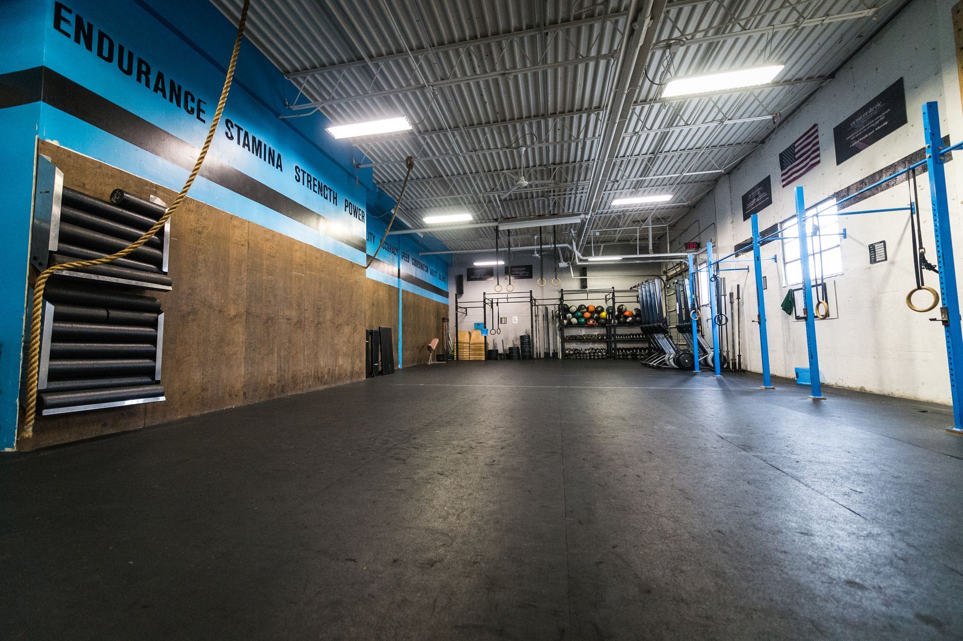 Empty crossfit gym with black floor, blue accents, and fitness equipment.