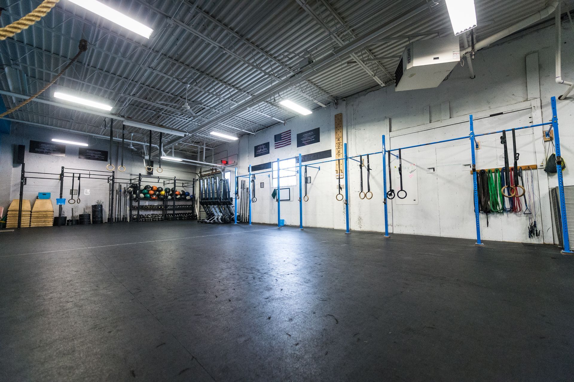 Gym interior with exercise equipment, including pull-up bars, weights, and gymnastic rings.