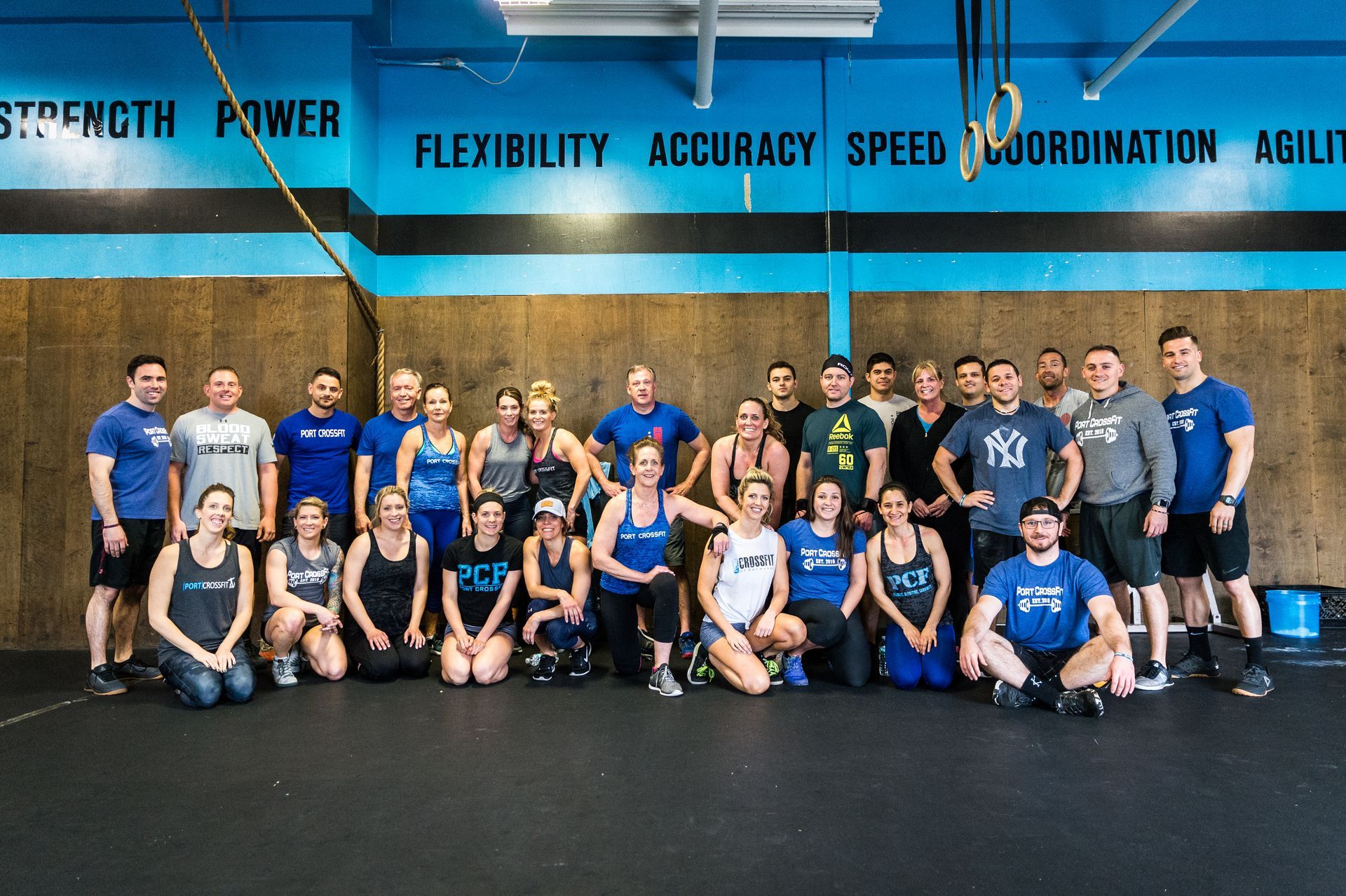 Group of people at a CrossFit gym, wearing workout clothes. Blue and black color scheme.