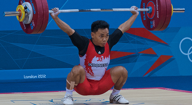 Weightlifter in red and white uniform, lifting a barbell overhead in the London 2012 Olympics.