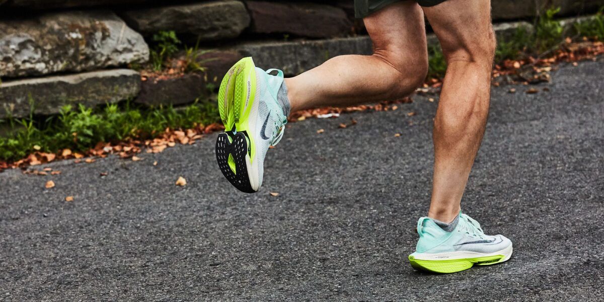 A runner's legs in motion on a paved road, wearing light blue and yellow running shoes.