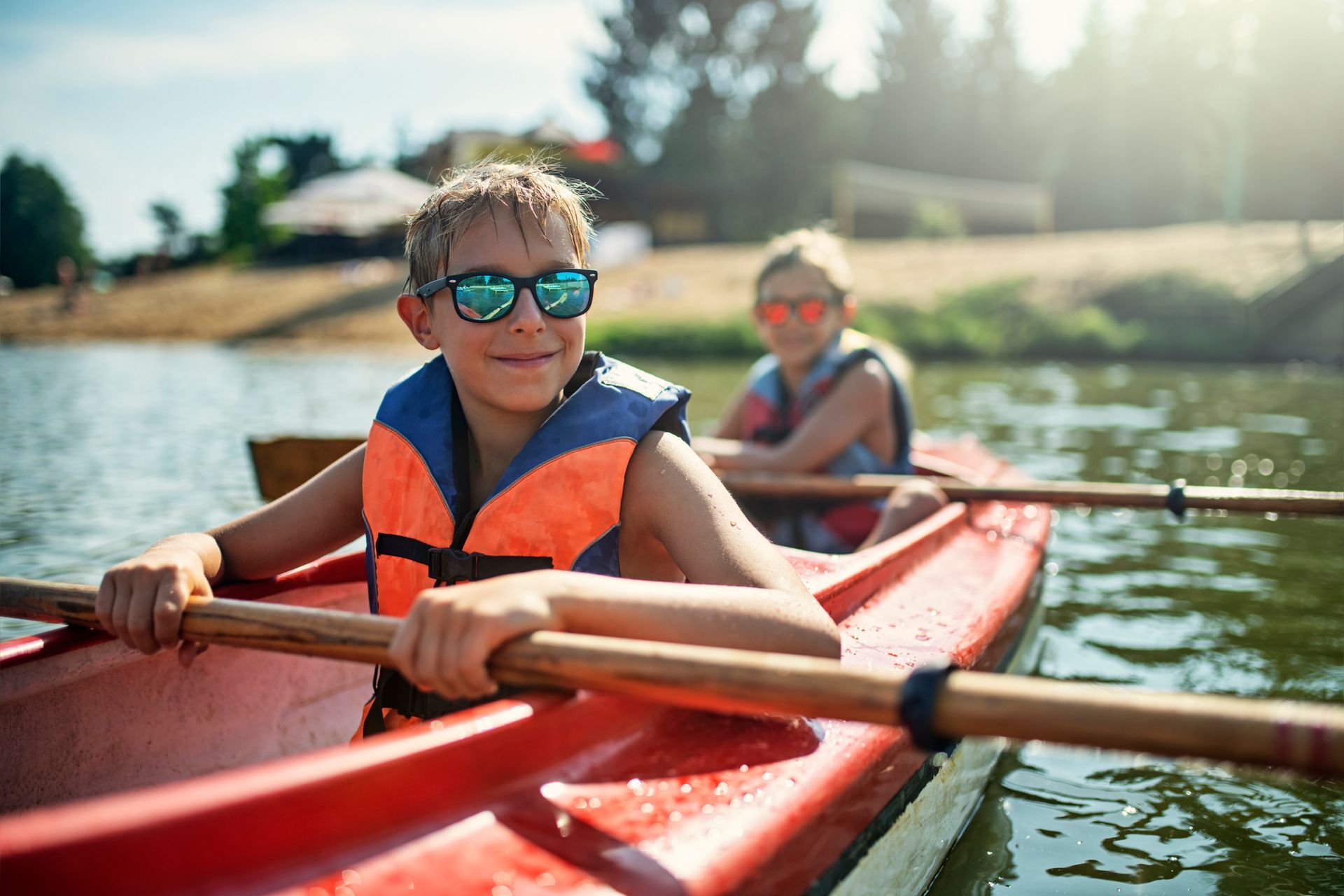Two boys happily kayaking across a calm, sparkling lake on a sunny day.