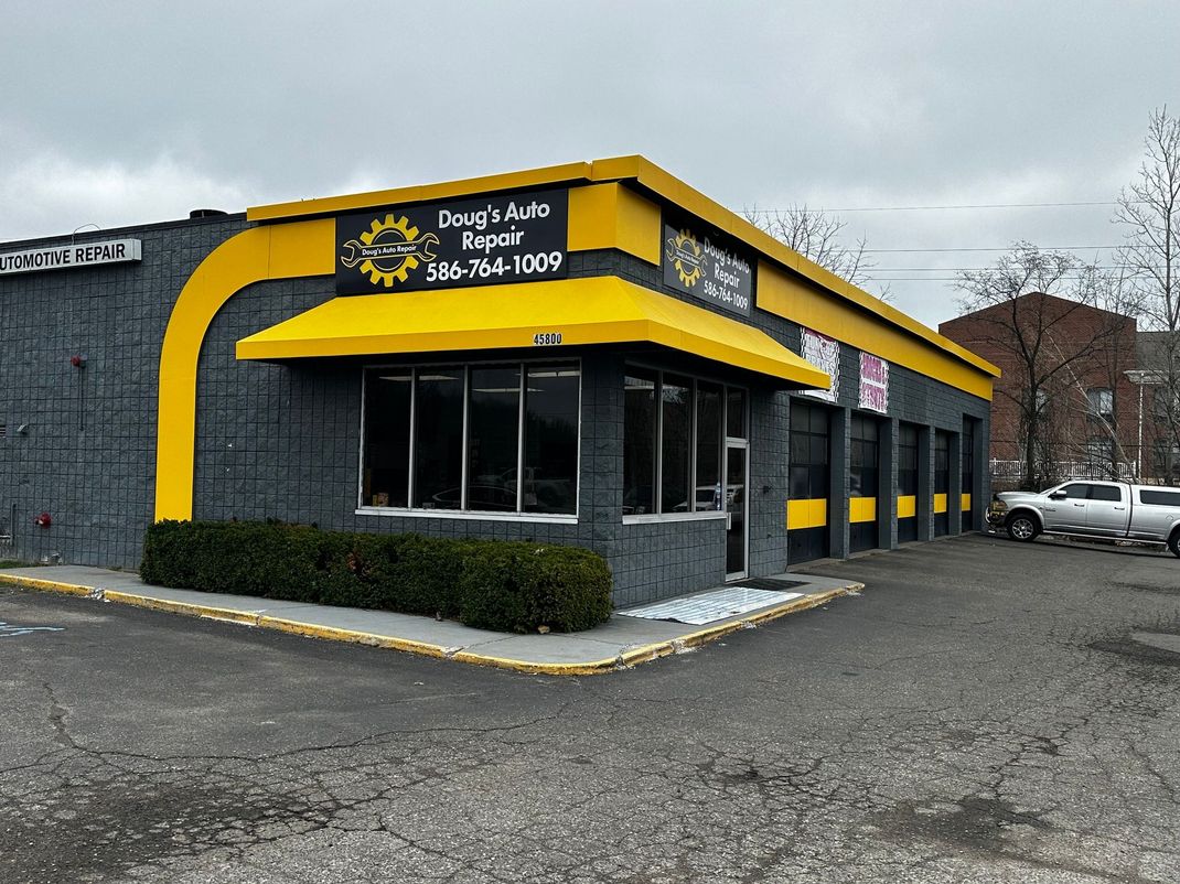Exterior of a gray and yellow auto repair shop with windows, a canopy, and a truck parked outside. | Doug’s Mobile Auto Repair
