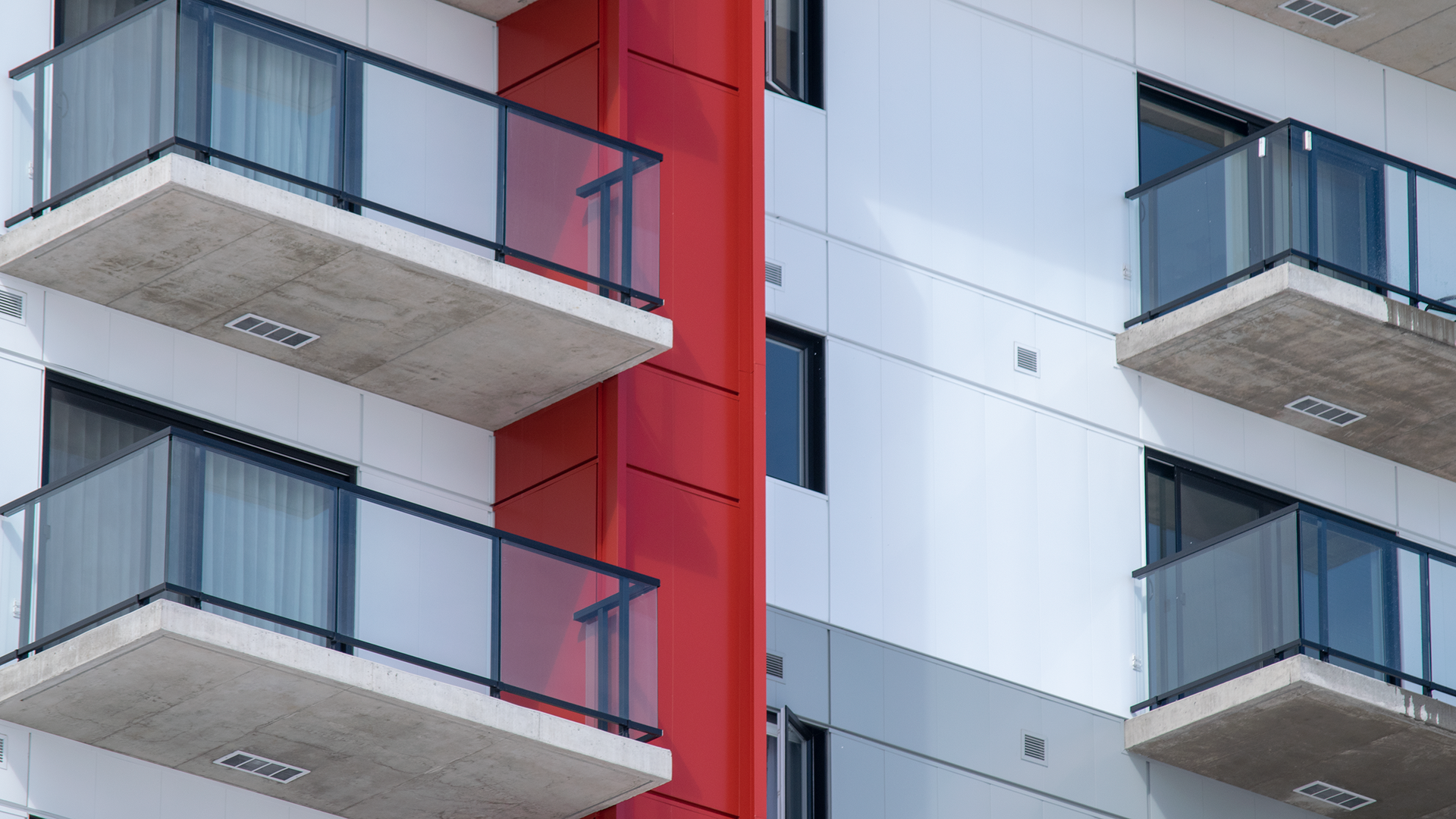 Extérieur d'un immeuble d'appartements moderne avec balcons; façade blanche, accent rouge, garde-corps en verre.
