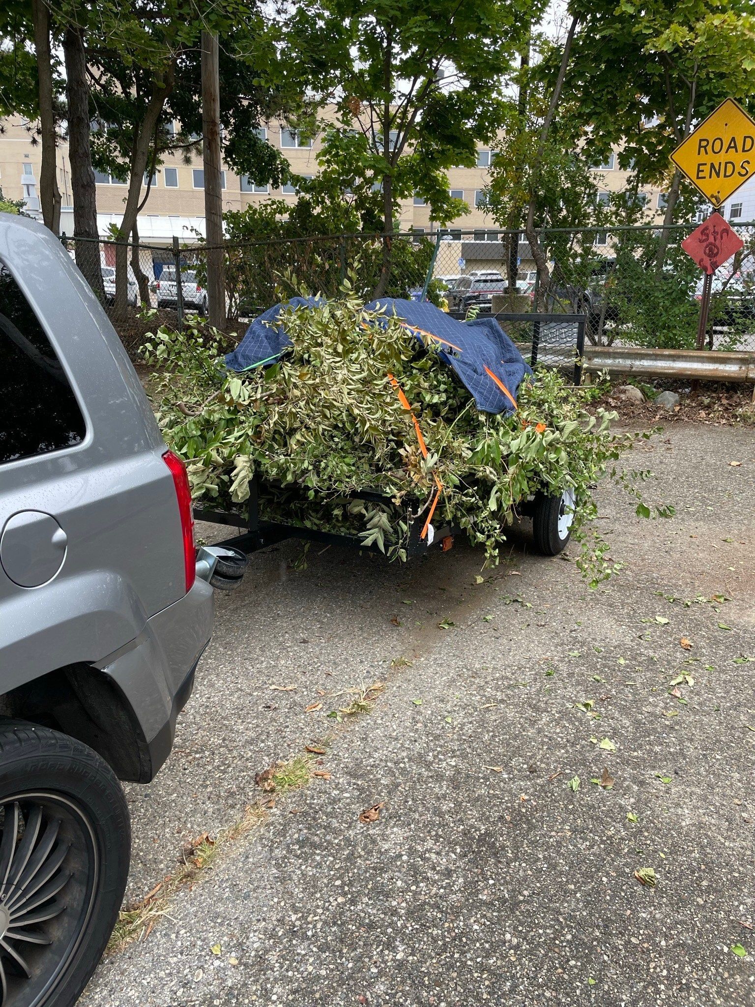 A car is parked in a parking lot next to a trailer filled with branches.
