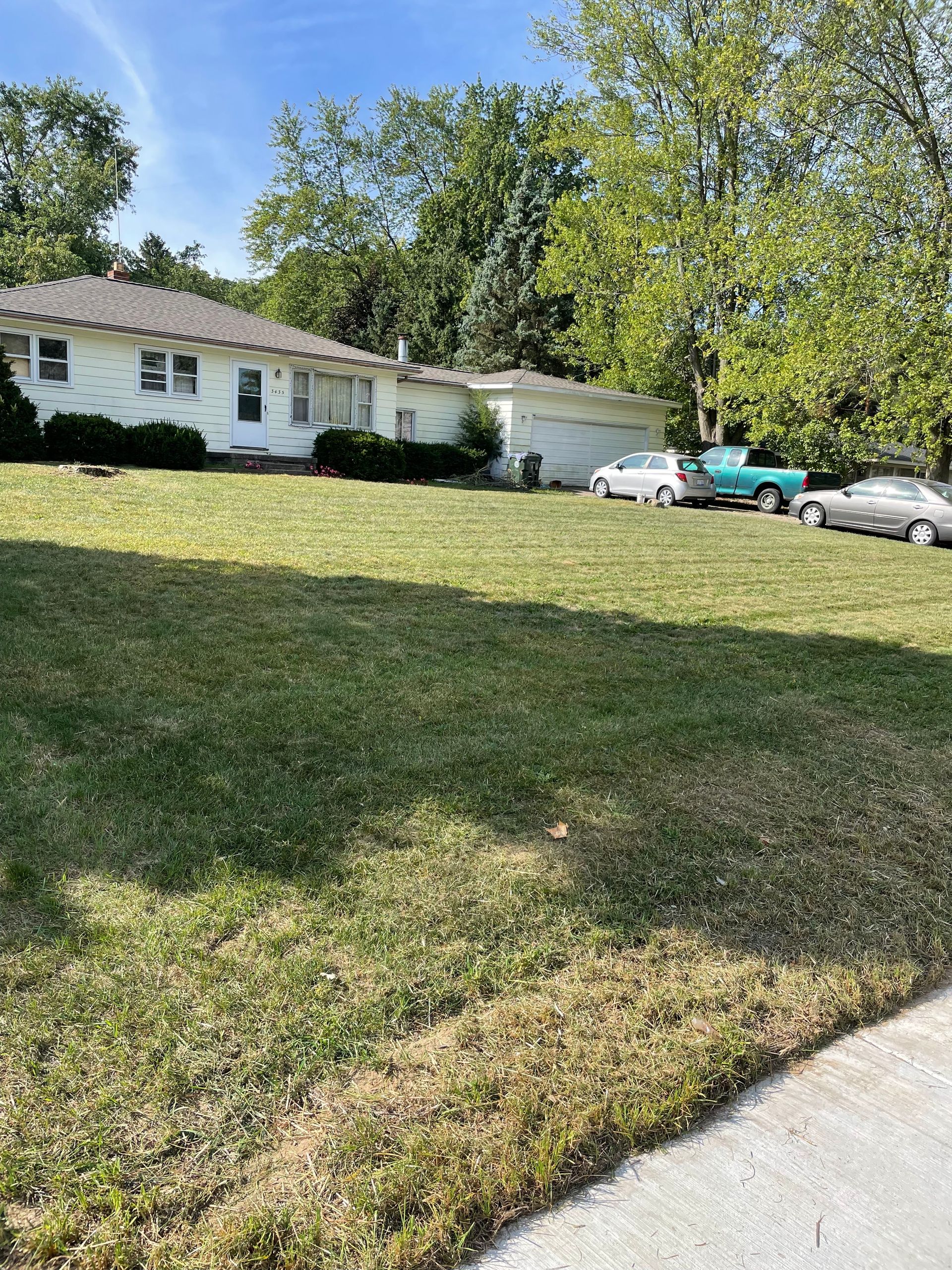 A house with a lot of grass and cars parked in front of it.